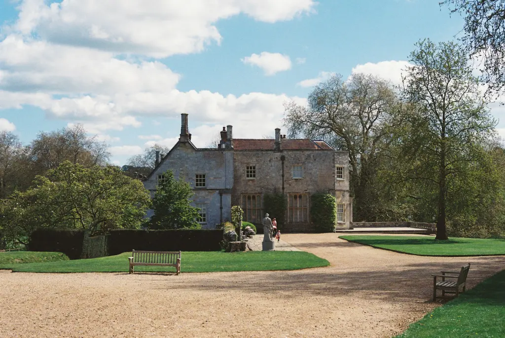 Stone country house in sunlit parkland with mature trees and a gravel forecourt