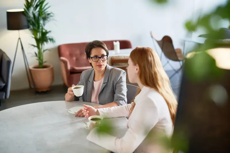 Two women in conversation over coffee, one listening attentively