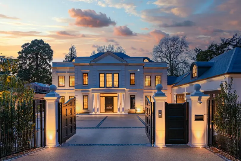 Newly built classical mansion at dusk, gates open, windows lit