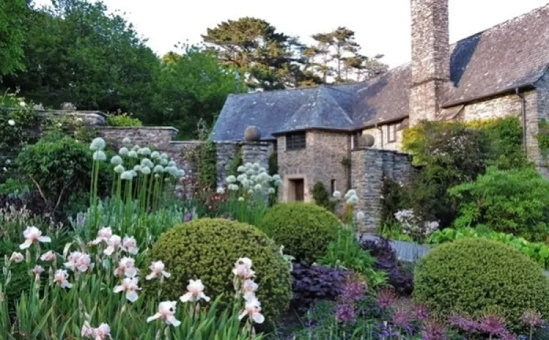 Stone country house behind a garden of irises, alliums and clipped box