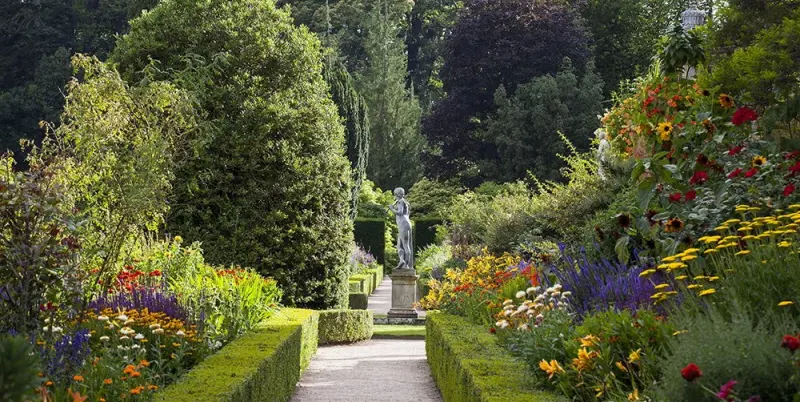 A gravel walk between herbaceous borders leading to a statue