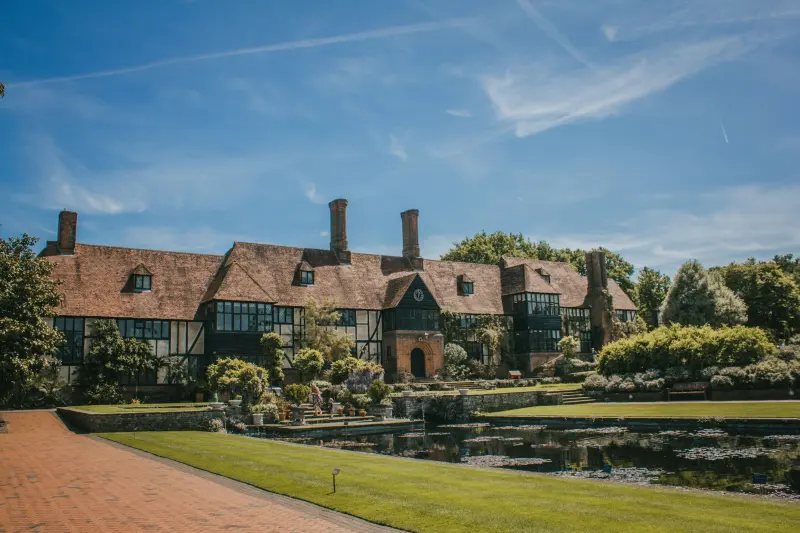 Half-timbered English manor house beside a lily pond on a summer day